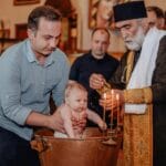 Stylizacje rodzinne na chrzciny i komunie – jak ubrać siebie i dziecko, żeby wyglądać elegancko i czuć się swobodnie Rodzinna ceremonia chrztu w kościele z księdzem zapalającym świece