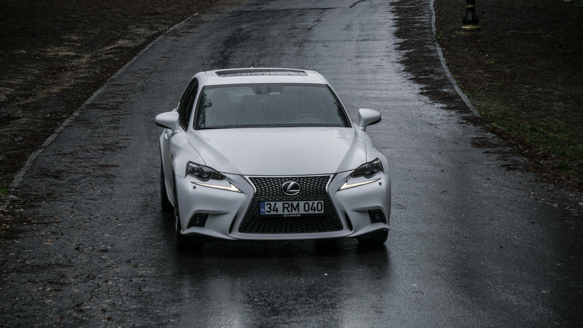 Biały Lexus z przodu jedzie po mokrej, deszczowej drodze