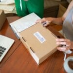 Dwie osoby pakujące zamówienia internetowe w małym sklepie z laptopem