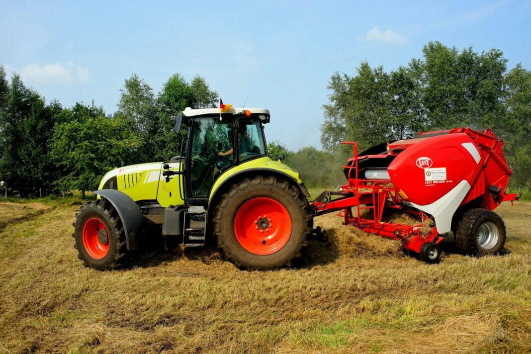 Zielony traktor z prasą do bel pracuje na polu otoczonym drzewami