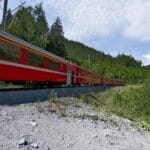 Czerwony pociąg jedzie przez zielone, górzyste tereny Szwajcarii