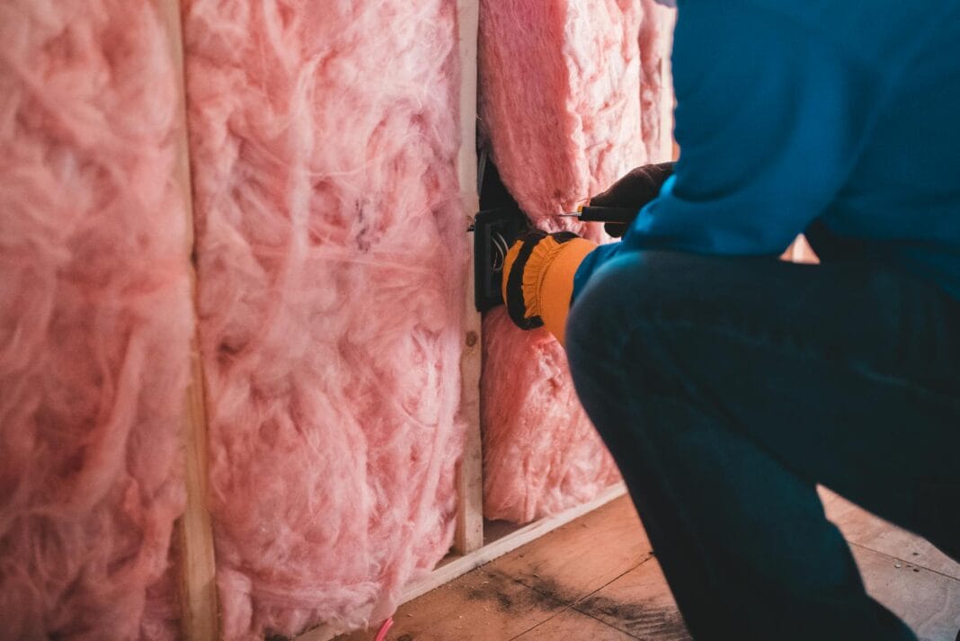 Pracownik w rękawicach montuje różową wełnę mineralną na ścianie Pracownik w rękawicach montuje różową wełnę mineralną na ścianie